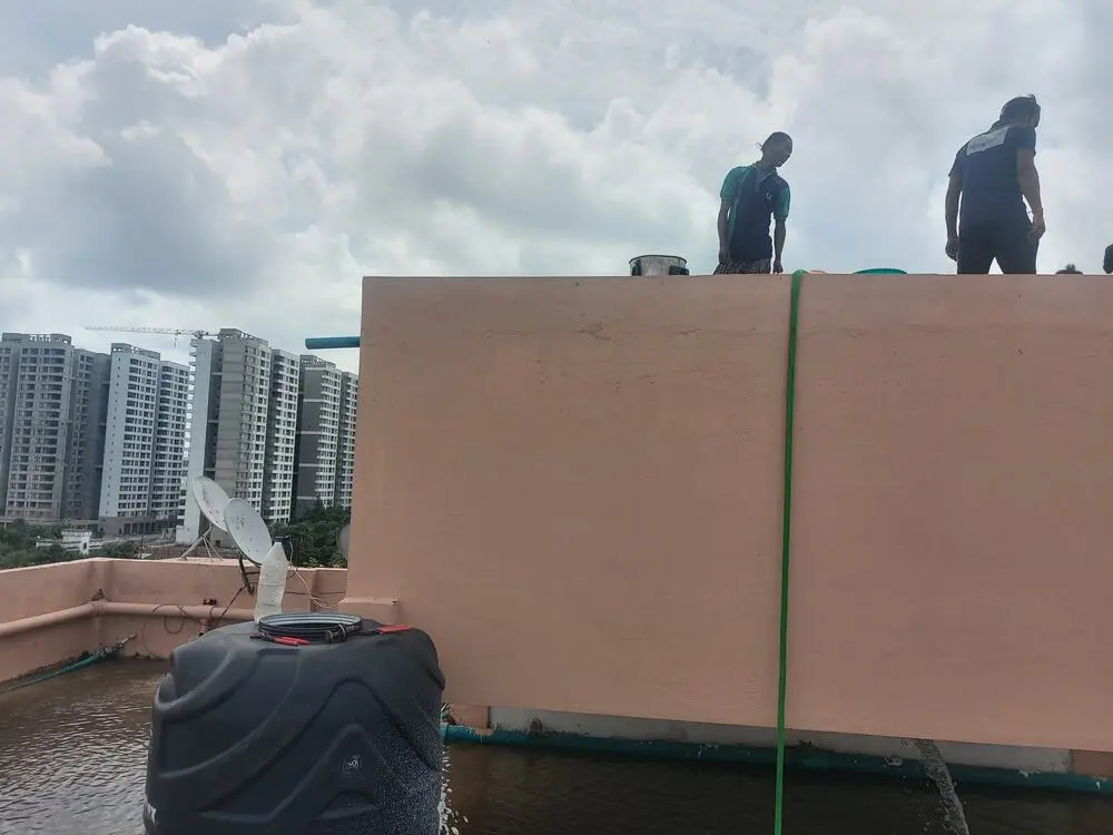 Two technicians on a rooftop overhead tank with high-rise buildings in the background